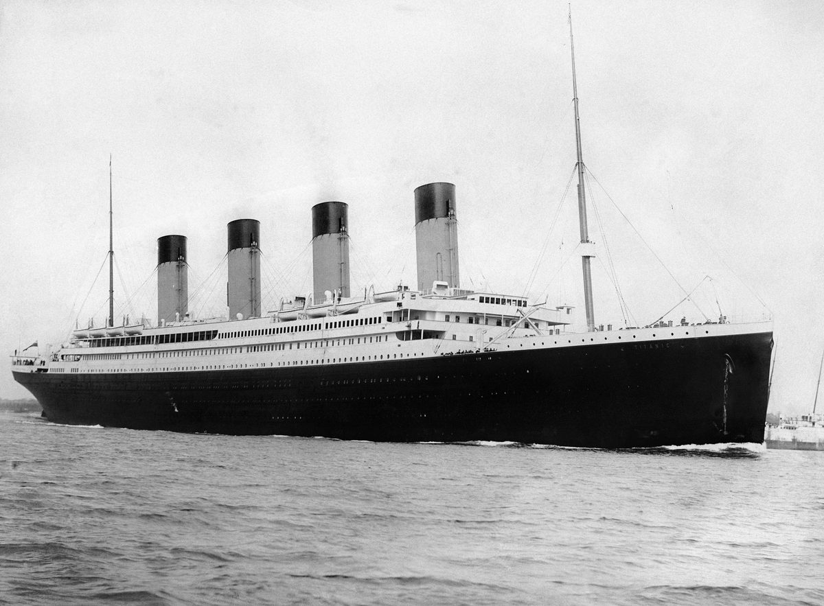 Black-and-white photograph of RMS Titanic under way, seen from the starboard bow with four funnels and a black hull